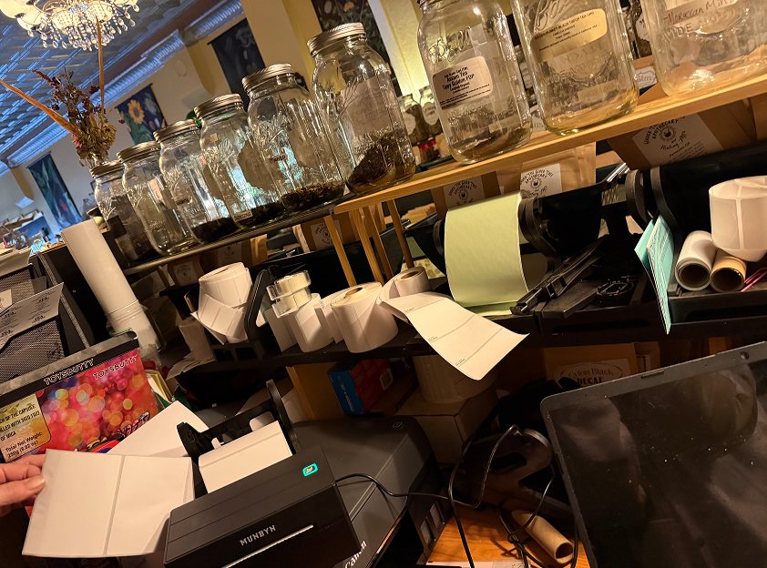 A small business workspace: label rolls in many sizes stacked on shelves around a label printer