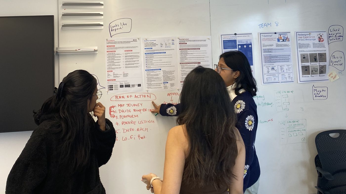 The IPD team reviewing concept posters and a plan of action on the studio whiteboard